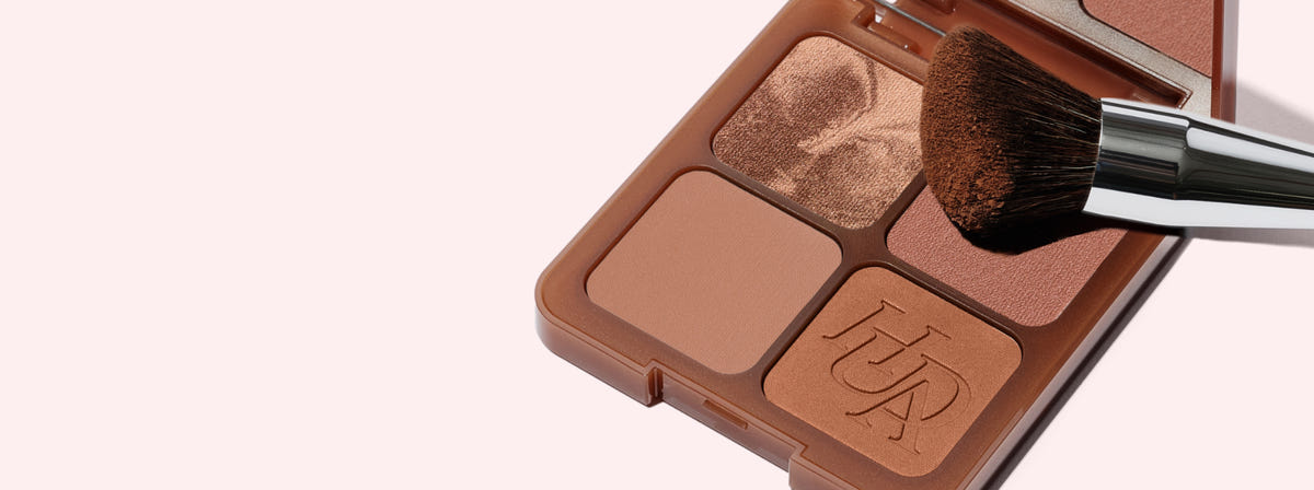 Huda Beauty banner for the Bronze Filter kits, open four-pan bronzer compact with a fluffy brush on a pale pink background