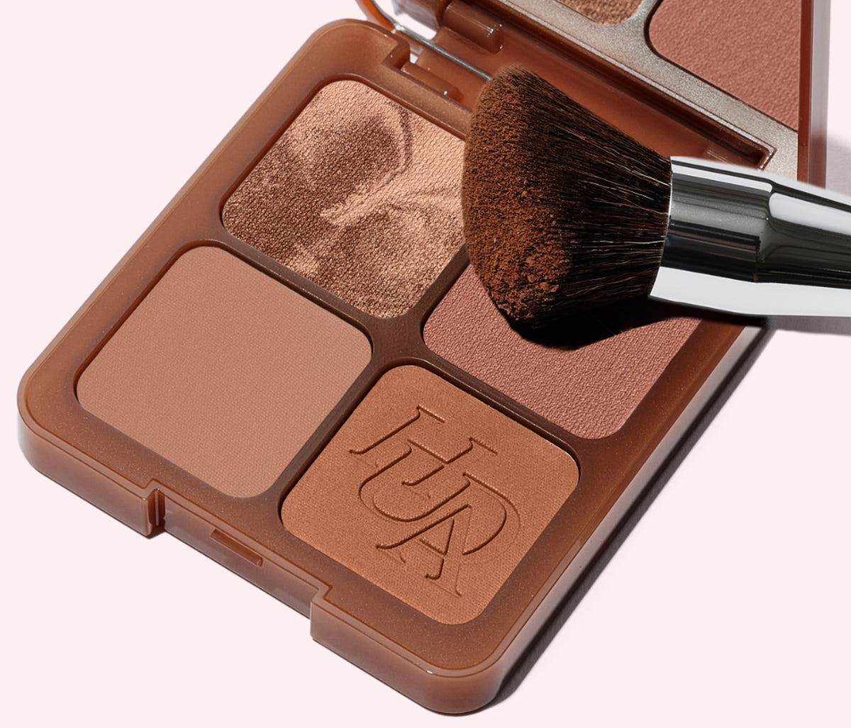 Huda Beauty banner for the Bronze Filter kits, open four-pan bronzer compact with a fluffy brush on a pale pink background