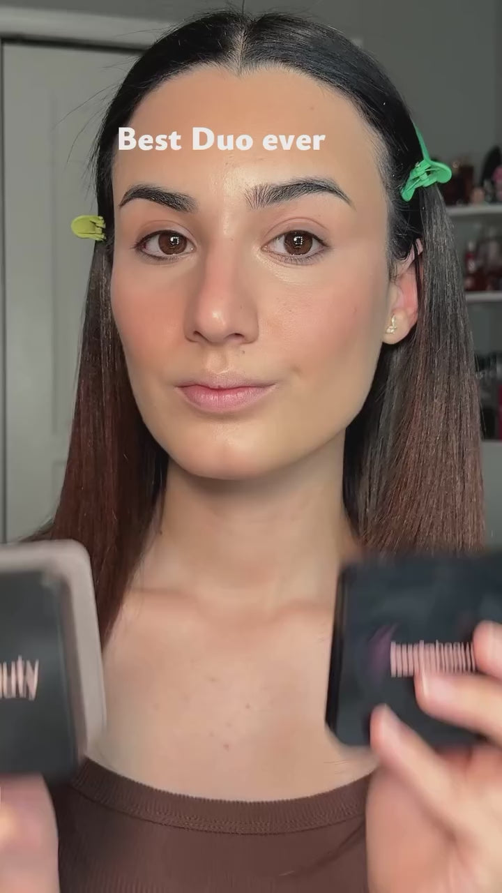 Woman presses loose powder under her eyes with a puff, finishes with a pressed powder compact, then holds up both Huda Beauty products.