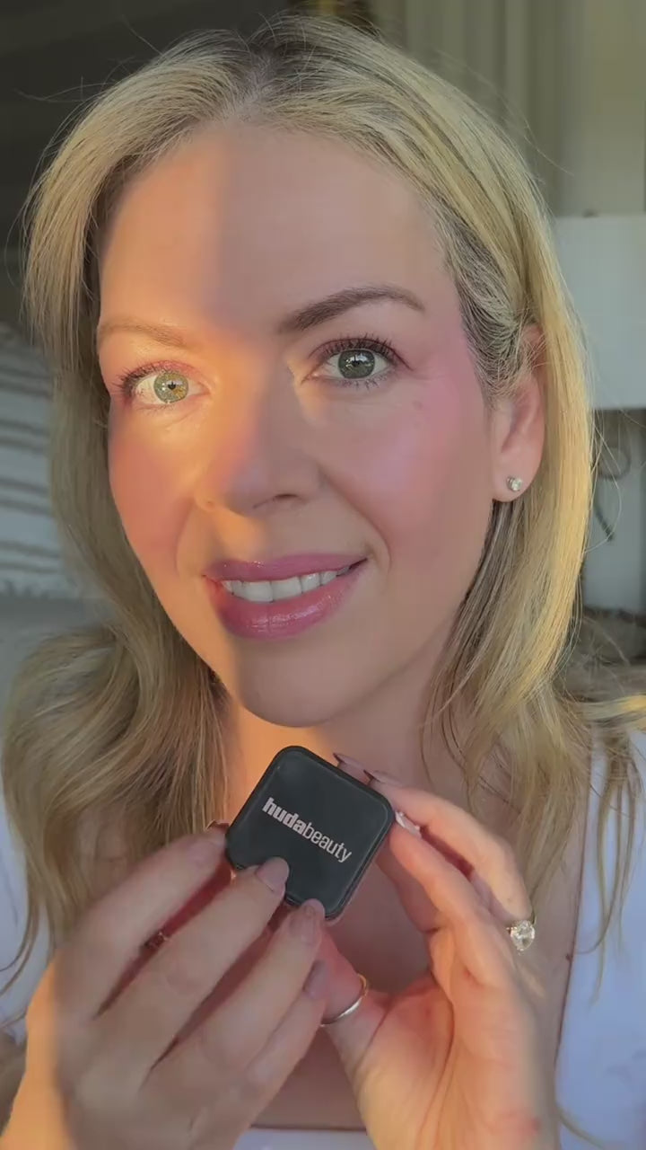 Woman dips a small brush into easy bake loose powder, presses it under her eyes and around her nose